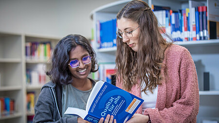 [Translate to English:] Zwei Studentinnen in der Campusbibliothek Mühldorf a. Inn schauen gemeinsam in ein Buch