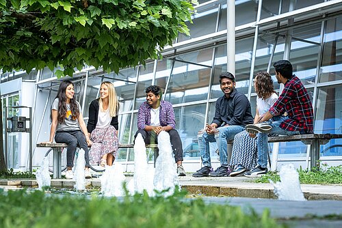 Studierende sitzen und unterhalten sich am Brunnen des Campus Rosenheim.