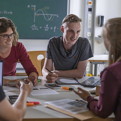 Vier Studierende sitzen an einem runden Tisch und tauschen sich zu Inhalten der Vorlesung aus