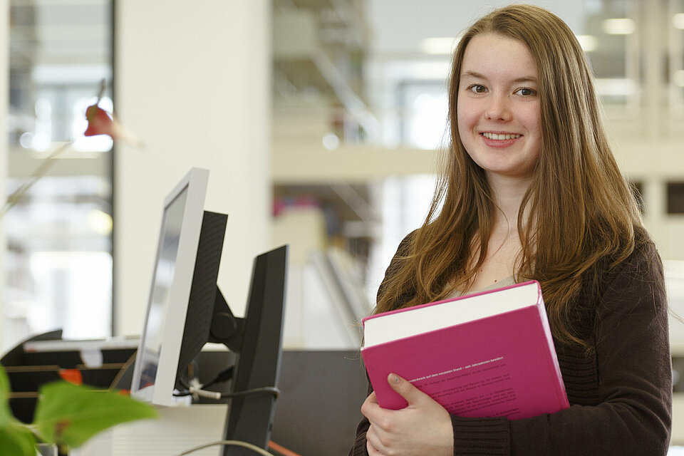 Eine Nutzerin im Informationsbereich der Bibliothek die ein großes Buch in den Händen hält.