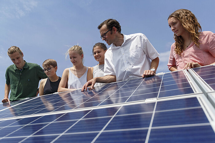 Das Bild zeigt Professor Frank Buttinger mit Studierenden auf einem Gebäude der Technischen Hochschule Rosenheim. Sie betrachten ein Solarmodul.
