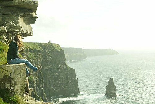 Studentin sitzt auf einer Steilklippe vor Irlands Küste