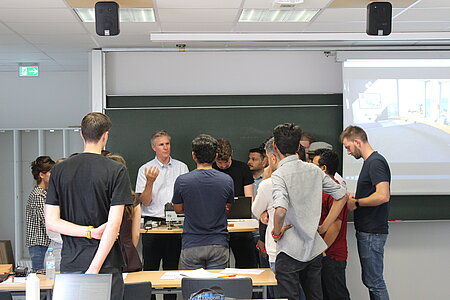 The lecturer and a group of students look at a component.