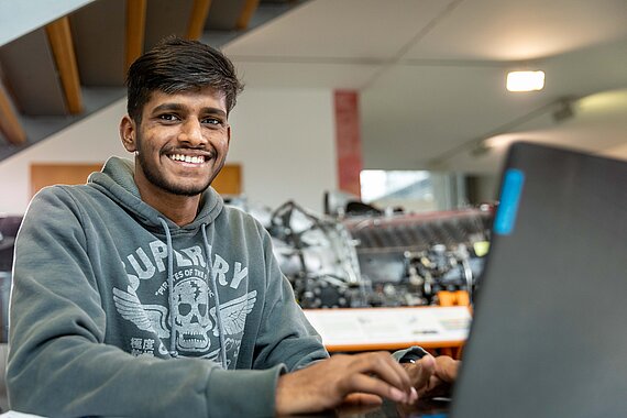 Student arbeitet an Laptop und schaut lächelnd in die Kamera