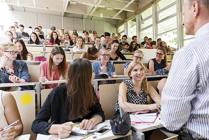 In einem Hörsaal sitzen Studentinnen und Studenten, die sich mit mit ihrem Professor austauschen