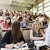 In einem Hörsaal sitzen Studentinnen und Studenten, die sich mit mit ihrem Professor austauschen