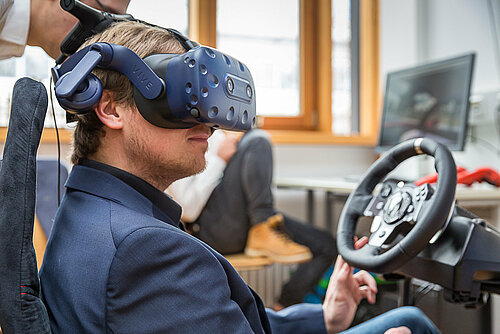 Student mit VR-Brille und Lenkrad beim Testen einer Simulation (Symbolbild des Studiengangs für Informatik))