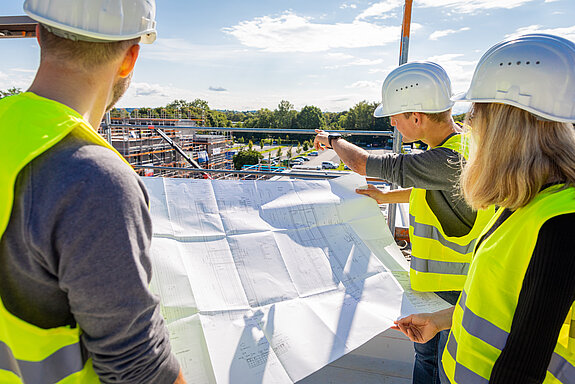 Personen auf einer Baustelle betrachten einen Bauplan