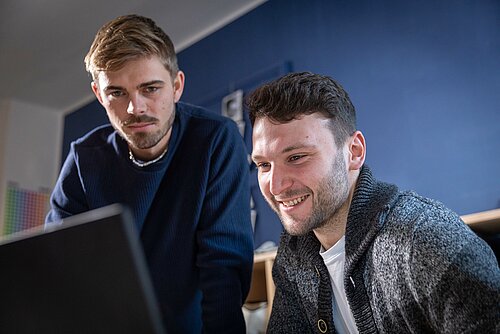 Zwei Studierende der TH Rosenheim auf Wohnungssuche schauen auf einen Laptopbildschirm.