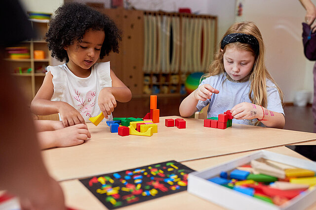 Zwei Kinder bauen aus bunten Holzklötzen Würfel und Türme
