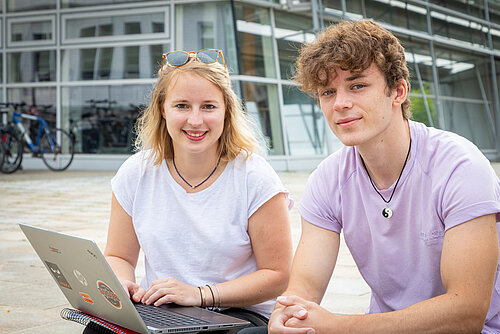 Studentin und Student mit Laptop vor einem Hochschulgebäude