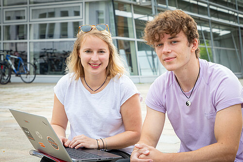 Student in front of a laptop on the steps in front of the S-Bau.