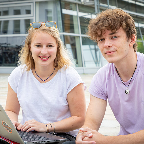 Studentin und Student mit Laptop vor einem Hochschulgebäude