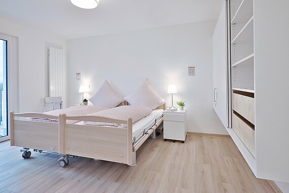 Blick in das Schlafzimmer im DeinHaus 4.0 Wohnkompetenzzentrum Freilassing mit schickem Pflegebett und unterfahrbaren Schränken