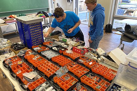 Das Bild zeigt zwei Studenten, die in einer Vielzahl von elektronischen Bauteilen etwas suchen.