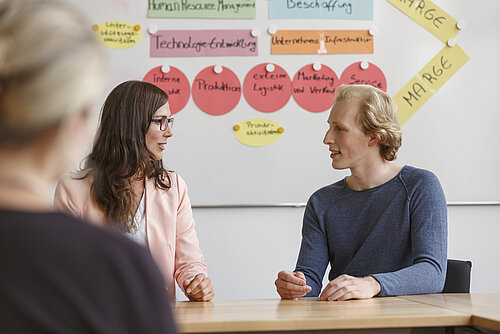 Drei Personen sitzen an einem Tisch und besprechen sich in einem Gremium.