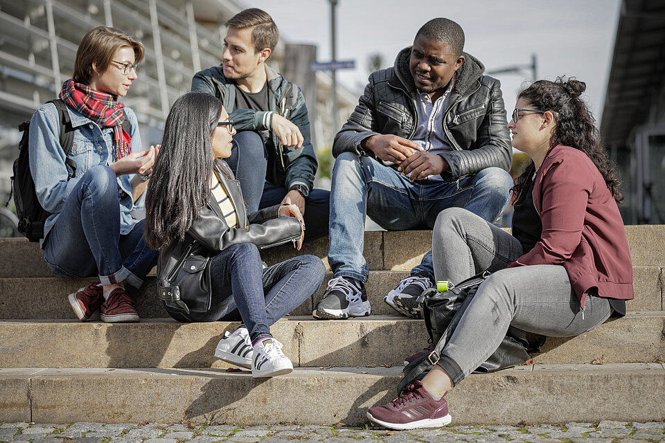 Das Bild zeigt Studierende, die auf einer Treppe am Campus Rosenheim sitzen.