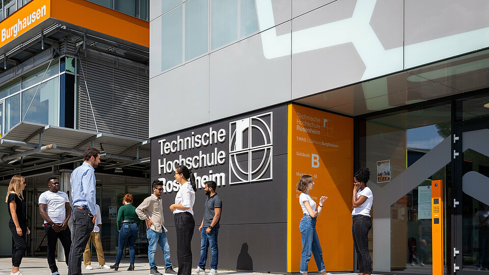 Students and a lecturer talking in front of the entrance to Campus Burghausen.