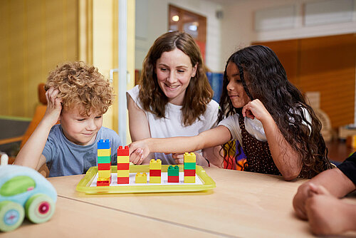 Pädagogin arbeitet mit einem Jungen und einem Mädchen mit Bausteinen am Tisch