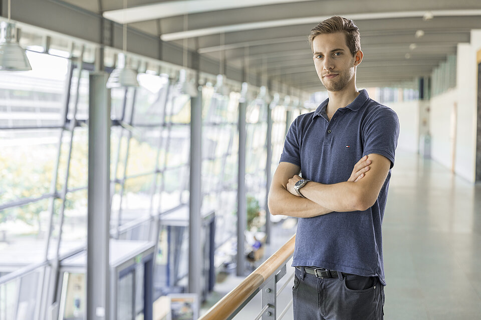 Student steht mit verschränkten Armen an Geländer