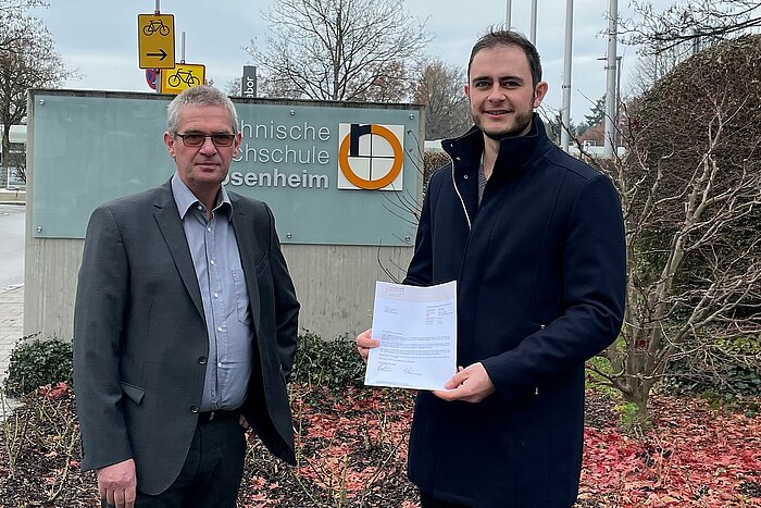 Auf dem Bild übergibt Prof. Dipl.-Ing. Peter Karlinger (links), Studiengangsleiter des Bachelorstudiengangs Kunststofftechnik, die Unterlagen des Stipendiums der Stahlgruber Gesellschafter Stiftung an den Masterstudenten Tobis Gemeiner (rechts).