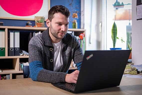 [Translate to English:] Student am Schreibtisch mit Laptop auf Jobsuche im Stellenportal