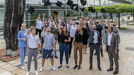 Business informatics graduates celebrate their graduation by throwing bachelor hats. 