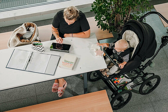 Studieren mit Kind: Studentin beim Lernen mit ihrem Kleinkind im Kinderwagen