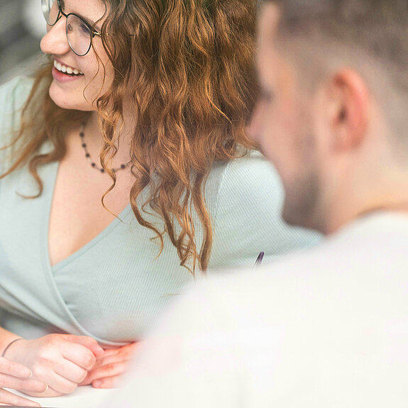 zwei Studentinnen und ein Student unterhalten sich am Tisch