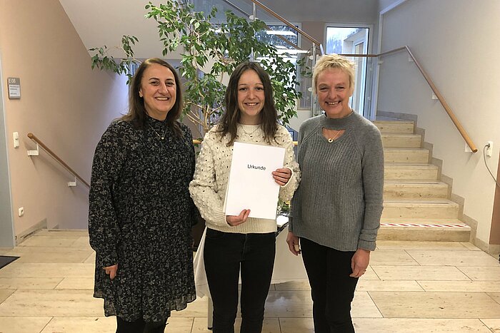 Auf dem Foto sind folgende Personen von links nach rechts zu sehen: Andrea Nallinger, stellvertretende Schulleiterin der RoMed-Berufsfachschule für Physiotherapie, Staatspreisträgerin Lea Rossmann, Prof. Dr. Sabine Ittlinger, Studiengangleiterin des Studiengangs Physiotherapie