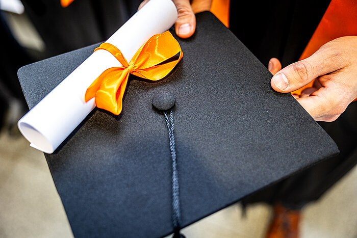 Das Bild zeigt Hände, die eine Mappe mit einer Promotionsurkunde halten.