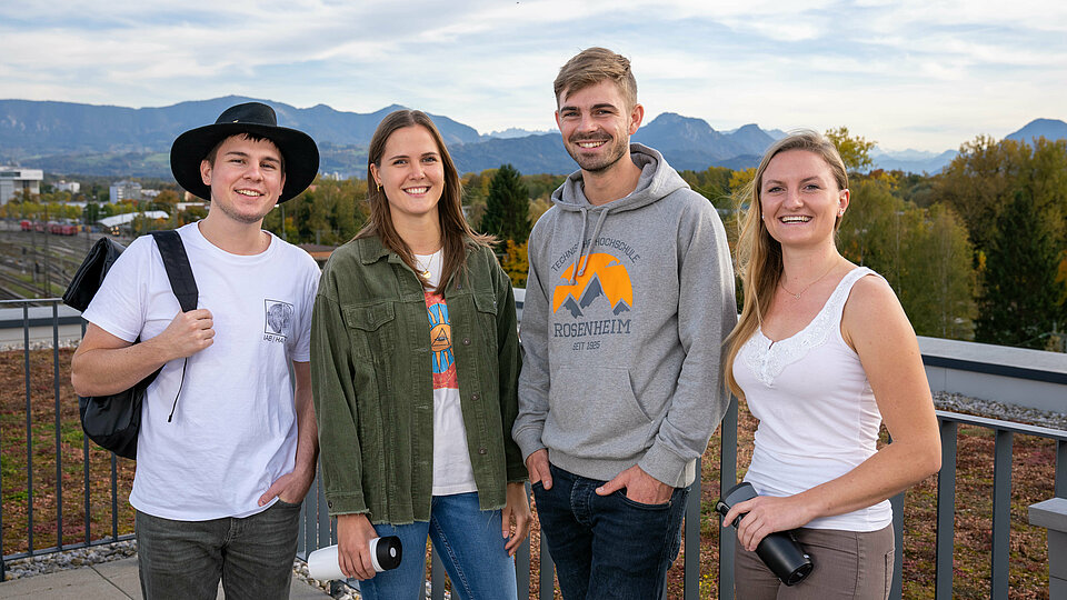 Vier fröhliche Studierende vor einem Bergpanorama.