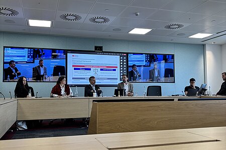 Boardmitglied Tadeu Cendon präsentiert vor einer digitalen Leinwand die Arbeitsweise des internationalen Gremiums der IASB. Neben ihm am Meetingtisch sitzen weitere Mitarbeiter des IASB.