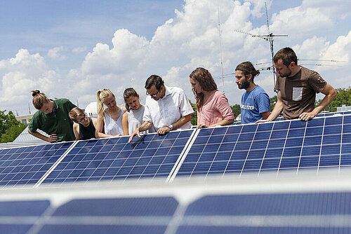 Studierende und ihr Dozent betrachten Solarzellen auf einem Dach.