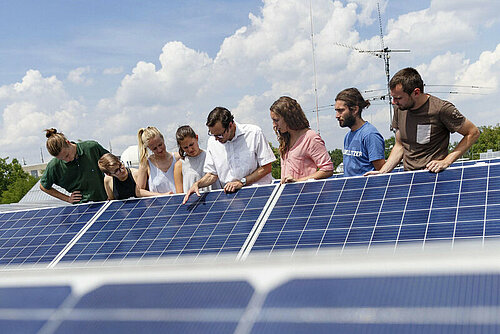 Students and their professor explore solar panels on a rooftop.