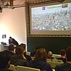Blick in den Hörsaal (von hinten zur Präsentation). Referent Florian Oelmaier lehnt am Dozentenpult und erläutert die gezeigten Folien rund um das Thema Industriespionage..