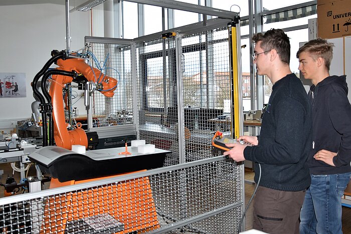 Das Bild zeigt zwei Schüler, die einen Roboter testen.