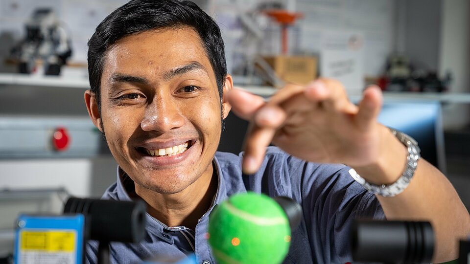 A student looks at a tennis ball balanced by a machine.