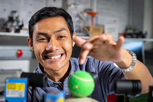 A student looks at a tennis ball balanced by a machine.