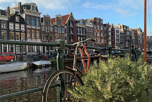 A bicycle leans against a railing. In the background is the backdrop of a city in the Netherlands.