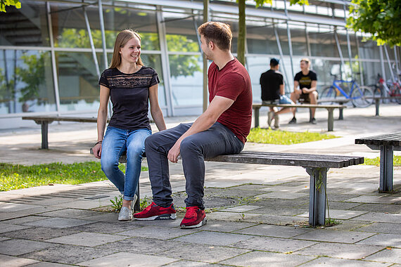 Female and male student talking on a bench