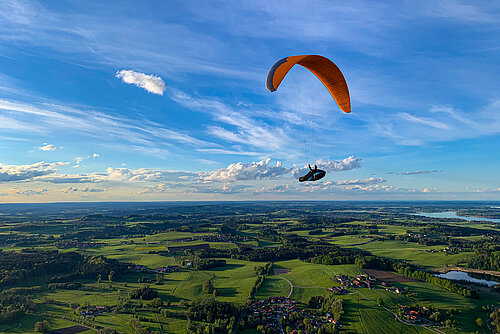 Fliegender Gleitschirmflieger mit Wäldern, grünen Wiesen und dem Chiemsee im Untergrund
