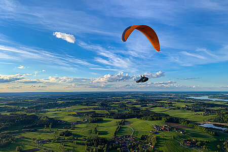 Fliegender Gleitschirmflieger mit Wäldern, grünen Wiesen und dem Chiemsee im Untergrund