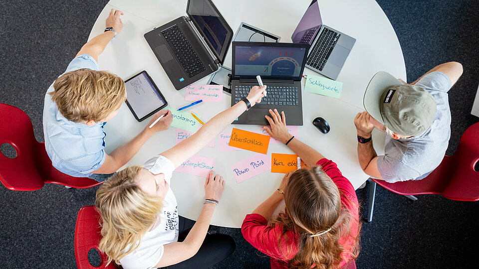 Blick von oben auf Vier Studierende, die an einem runden Tisch arbeiten