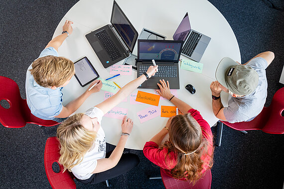 Blick von oben auf Vier Studierende, die an einem runden Tisch arbeiten