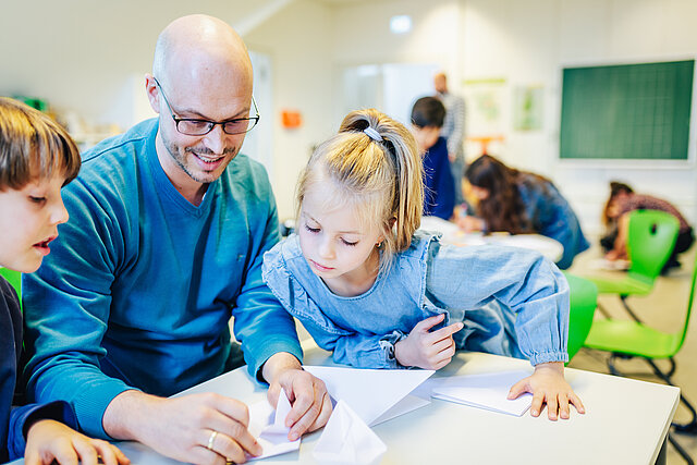 Ein Erzieher faltet mit zwei Kindern Papier