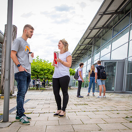 Studierende unterhalten sich in zweier und dreier Gruppen auf einem Vorplatz der Hochschule