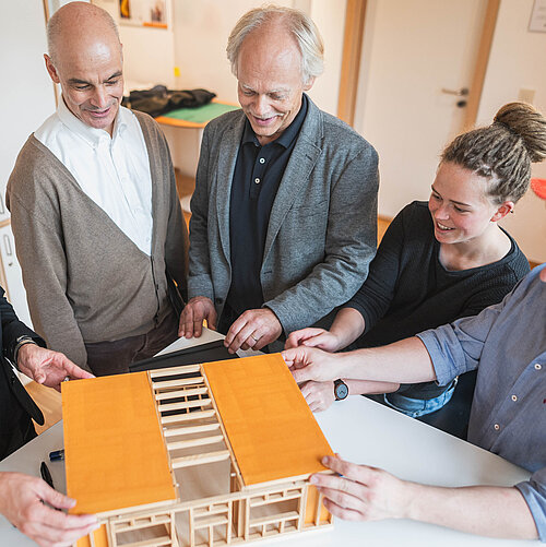 Professoren und Studierende vor Modell aus Holz