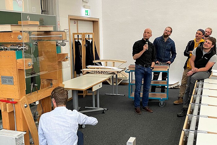 Das Bild zeigt Studenten, deren Modellbrücke auf einem Prüfstand einem Belastungstest unterzogen wird.
