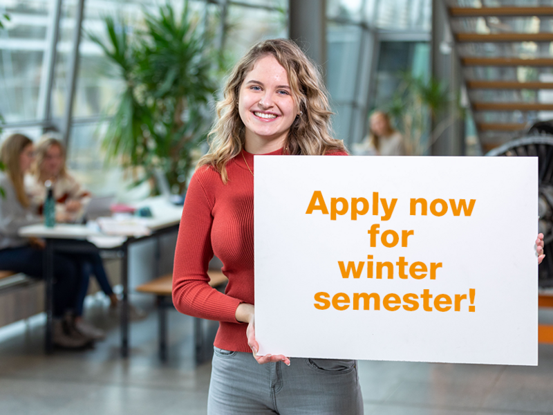 student holding a sign saying apply now for winter semester